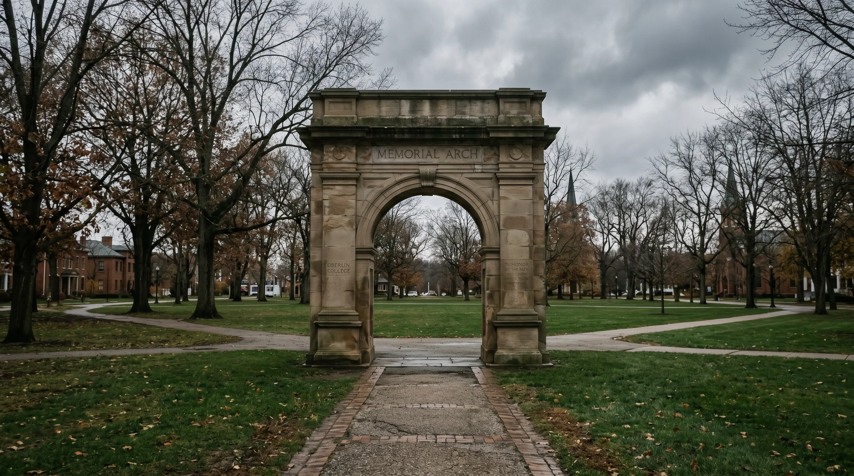 the Memorial Arch and tree-lined open green of Tappan Square in downtown Oberlin, sandstone arch in mid-ground, mature trees framing the square
