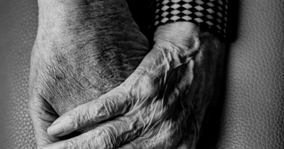 An elderly woman sitting alone by a window in a long-term care facility