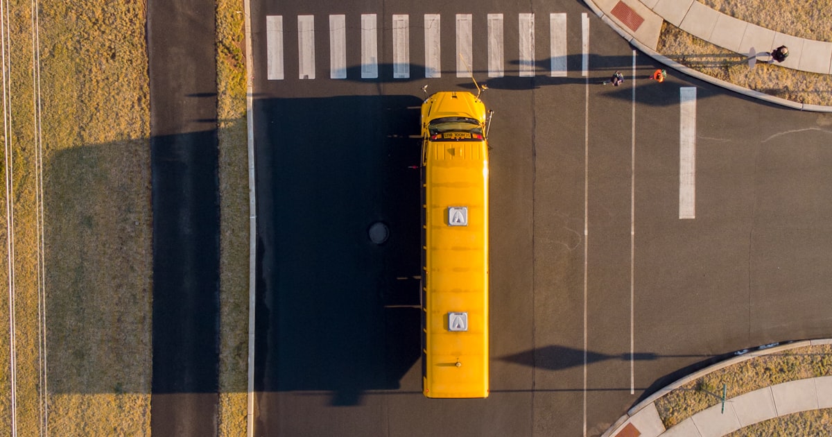 A parent and child waiting to cross a Cleveland street near a school during morning traffic