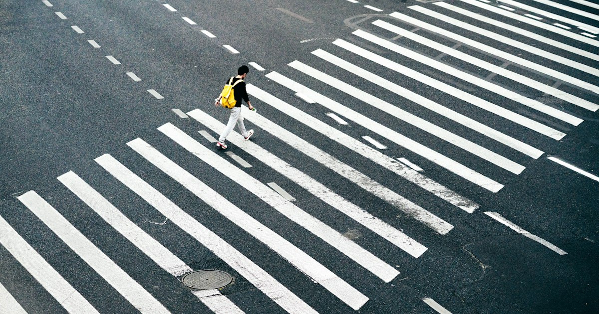 Person walking across an urban intersection at night as headlights approach