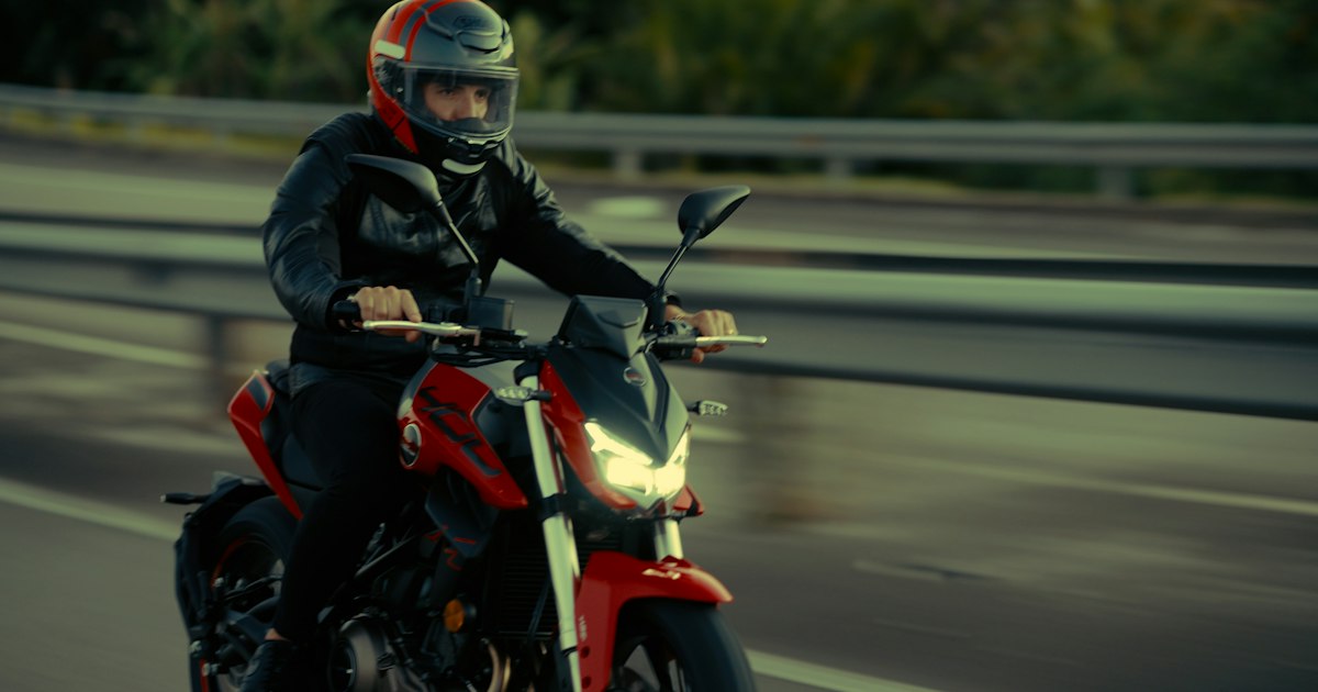 A rider on a red motorcycle traveling a two-lane road