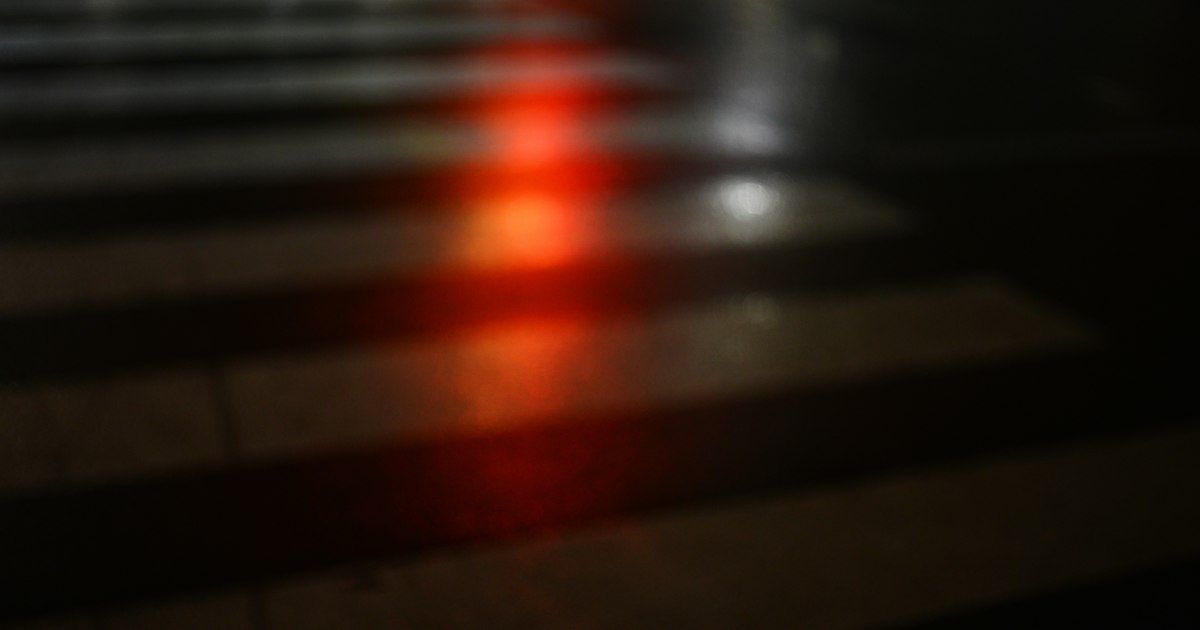 A red traffic light reflecting on a dark, wet crosswalk at night