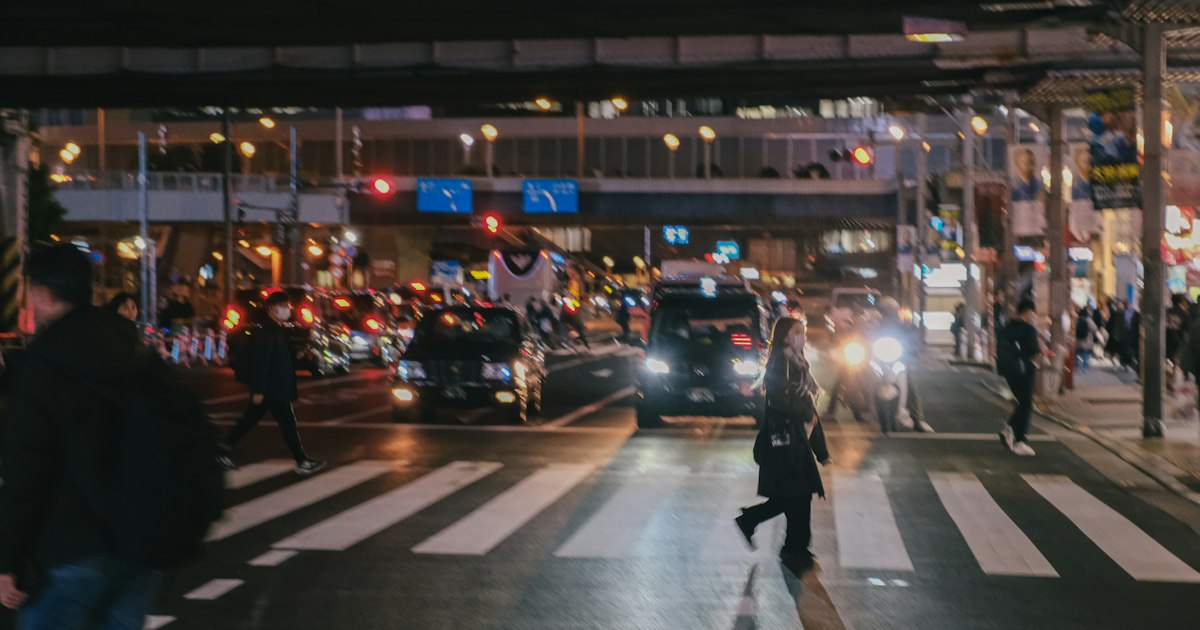 People crossing a busy Cleveland street under streetlights at night