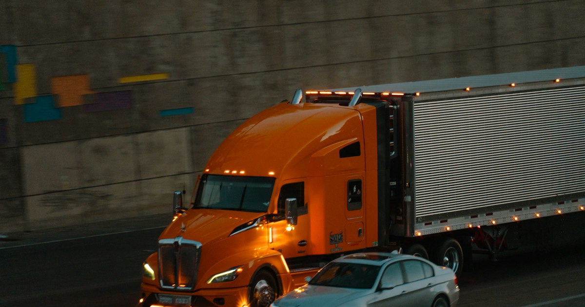 An orange semi-truck and a passenger car sharing a dark Ohio highway during the evening commute